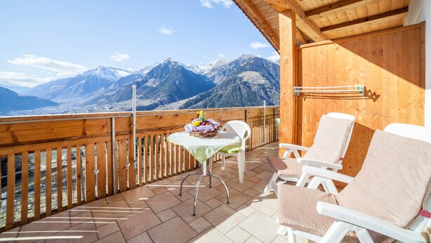 Un balcon en bois, agrémenté d’une table et de chaises, qui offre une vue sur une chaîne de montagnes.
