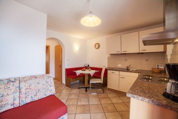 A compact kitchen with a dining area, a sofa, and a clock on the wall.