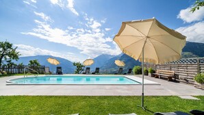 A swimming pool with lounge chairs and umbrellas, surrounded by a wooden fence and mountains in the background. - Apartment 'Roath Hof 3' with Mountain View, Shared Garden and Wi-Fi (Schenna)