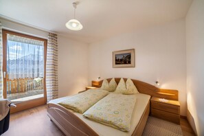 A bedroom with a bed, bedside tables, a nightstand, a window with curtains, a picture on the wall, and a view of the outside.