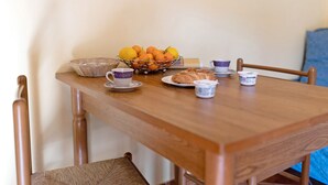 Een houten eettafel met een mand sinaasappels, een bord croissants en twee kopjes op schotels.