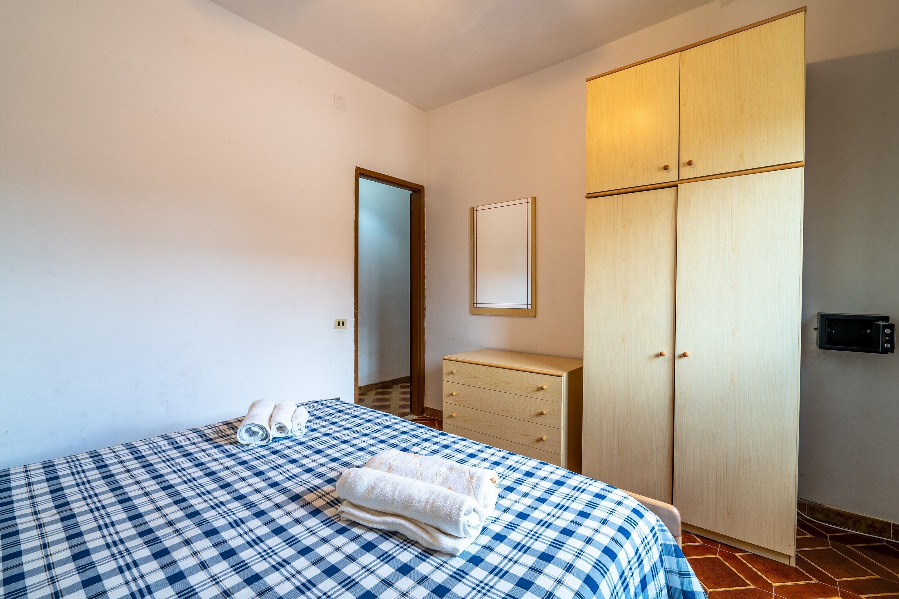 Une chambre à coucher comprenant un lit, une armoire en bois, une petite commode et un miroir.