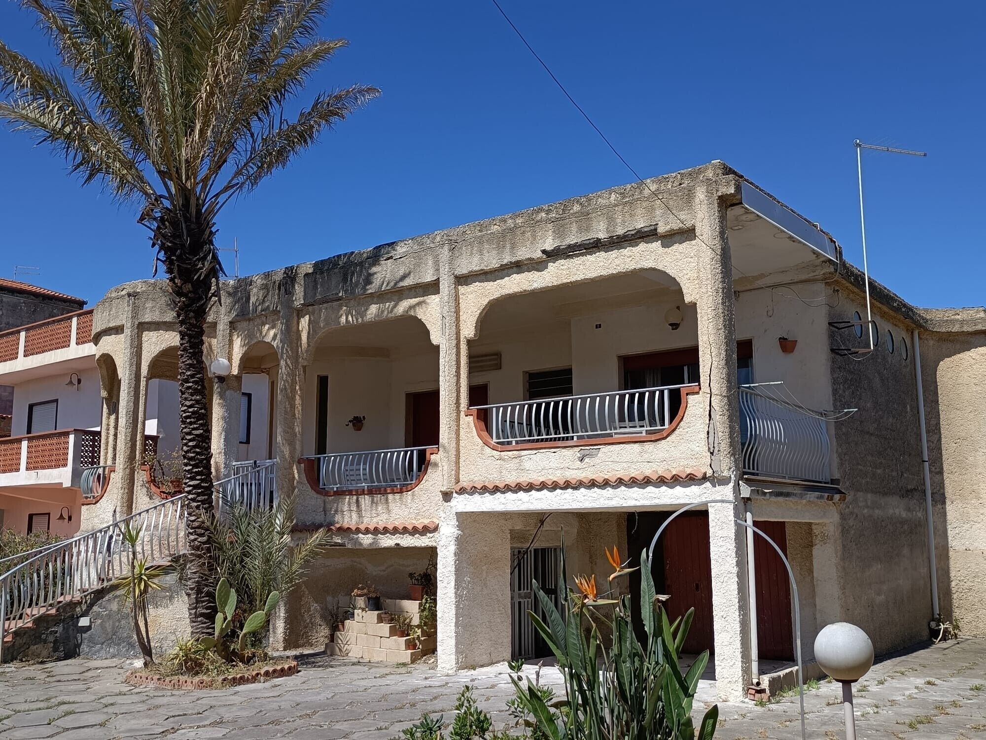 Un edificio con un balcone, una scala e una palma.