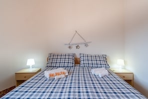 Un lit recouvert d’une couvre-lit à carreaux, deux tables de chevet avec des lampes et un élément décoratif fixé au mur.