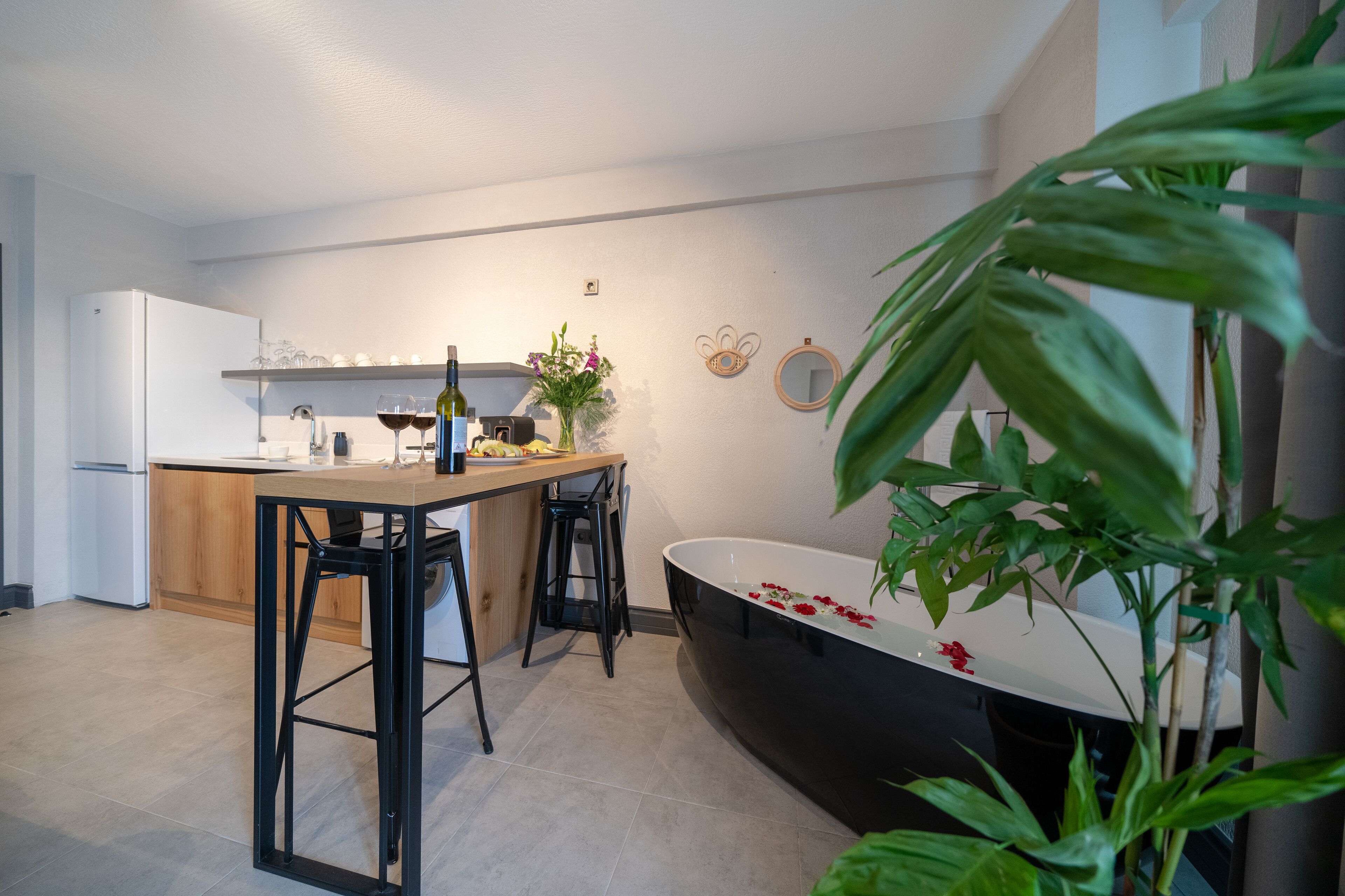 A modern kitchen with a dining area, a black bathtub, and a large green plant.
