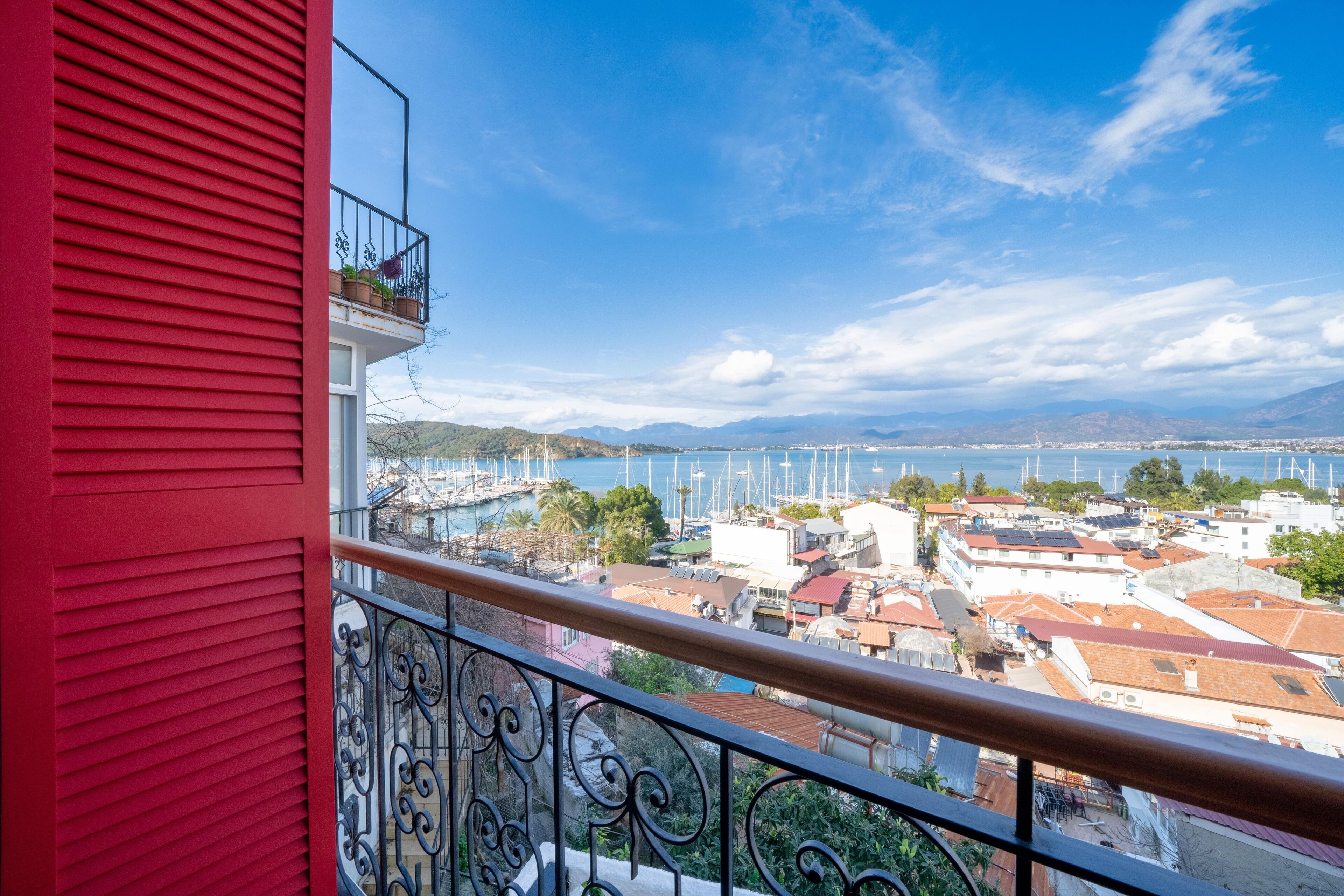 Ein Balkon mit roter Wand, der auf einen Yachthafen mit Booten und Gebäuden blickt.