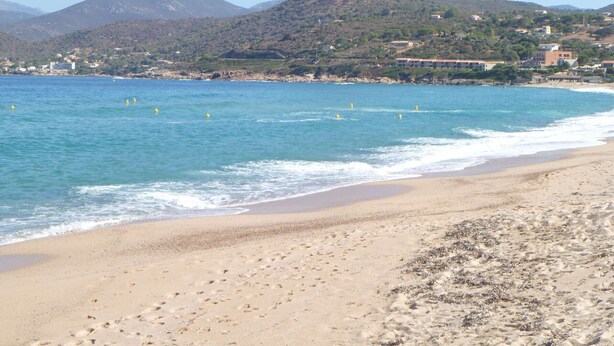 A beach with clear blue water, sandy shore, and a mountain in the background.