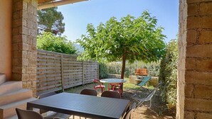 A covered patio area with a table and chairs, a wooden fence, and a tree.