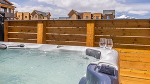 A hot tub with two glasses, surrounded by wooden fencing, and houses in the background. - Luxury condo w/private hot tub & Lone Peak Views, minutes to Big Sky Resort - Copper John Getaway (Big Sky)