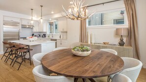 A modern kitchen with white cabinets, a stainless steel refrigerator, and a wooden dining table with a bowl of fruit. - Luxury condo w/private hot tub & Lone Peak Views, minutes to Big Sky Resort - Copper John Getaway (Big Sky)