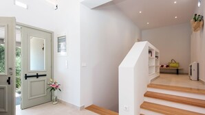 A modern interior with a staircase, a door, and a small shelf with books and a handbag. - Villa Helonaki (CORFU)