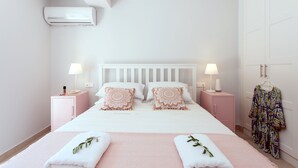 A neatly arranged bedroom with a white bed, two bedside tables, a pink wardrobe, and a hanging garment. - Villa Helonaki (CORFU)