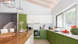 A modern kitchen with green cabinets, a wooden countertop, and a large window. - Villa Helonaki (CORFU)
