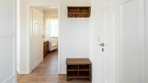 A hallway with white walls and wooden flooring, leading to a bedroom with a bed and a dresser.