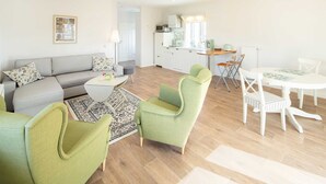 A modern living room with a sofa, green armchairs, a coffee table, and a dining table with chairs.