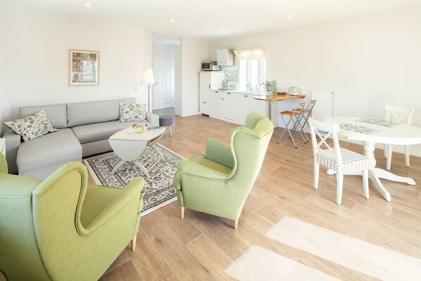 A modern living room with a sofa, green armchairs, a coffee table, and a dining table with chairs.