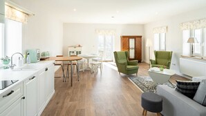 A modern kitchen with white cabinets, a dining area with a round table and chairs, a green armchair, and a grey sofa.