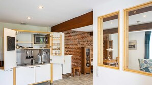 A compact kitchen with modern appliances, a brick wall, and a dining area with a table and chairs. - Mauersegler - Old Castle Brewery Apartments (Bad Wildungen)