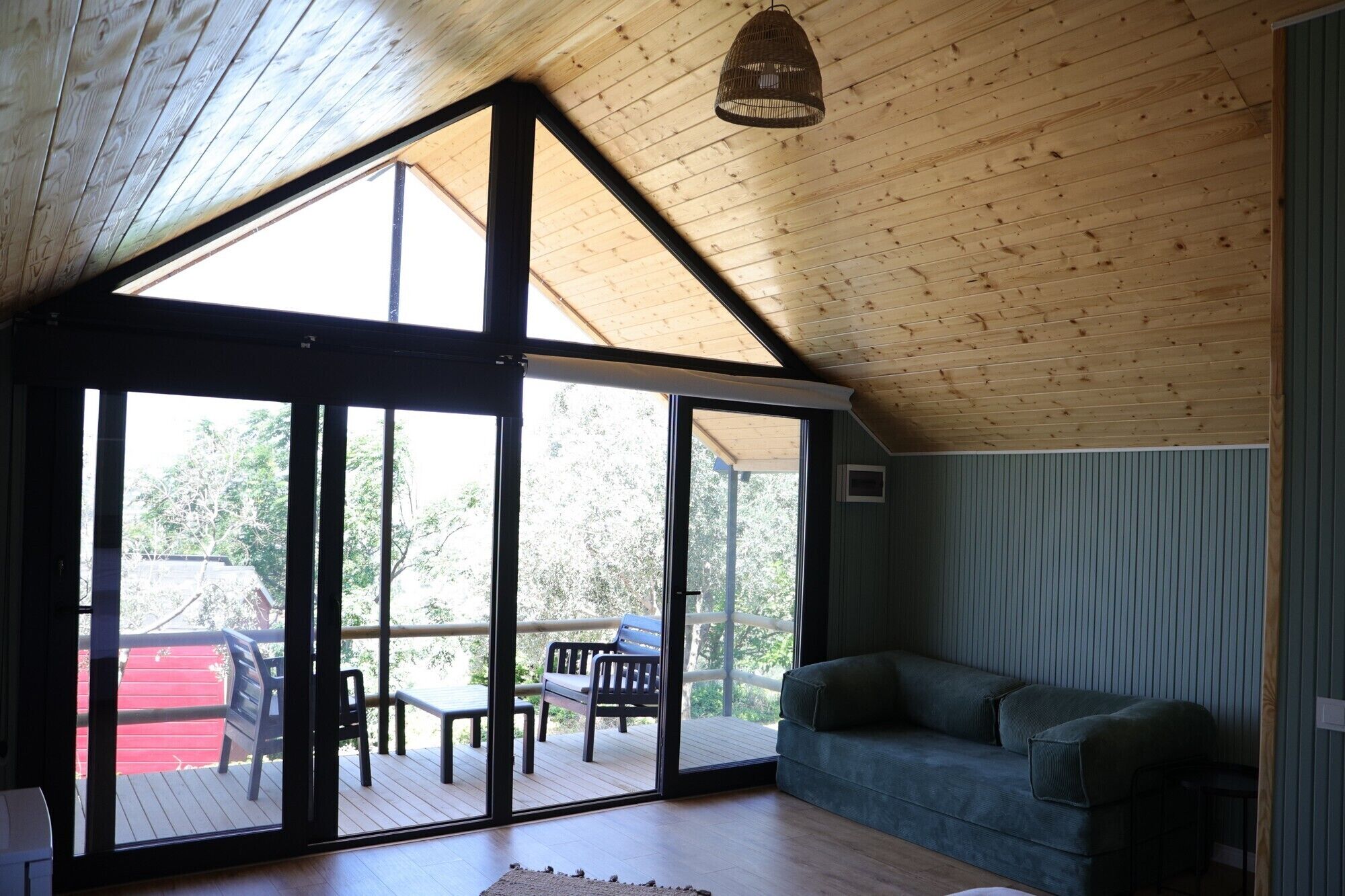 Una habitación con techo de madera, grandes puertas correderas de vidrio que dan a una terraza exterior y un sofá verde.