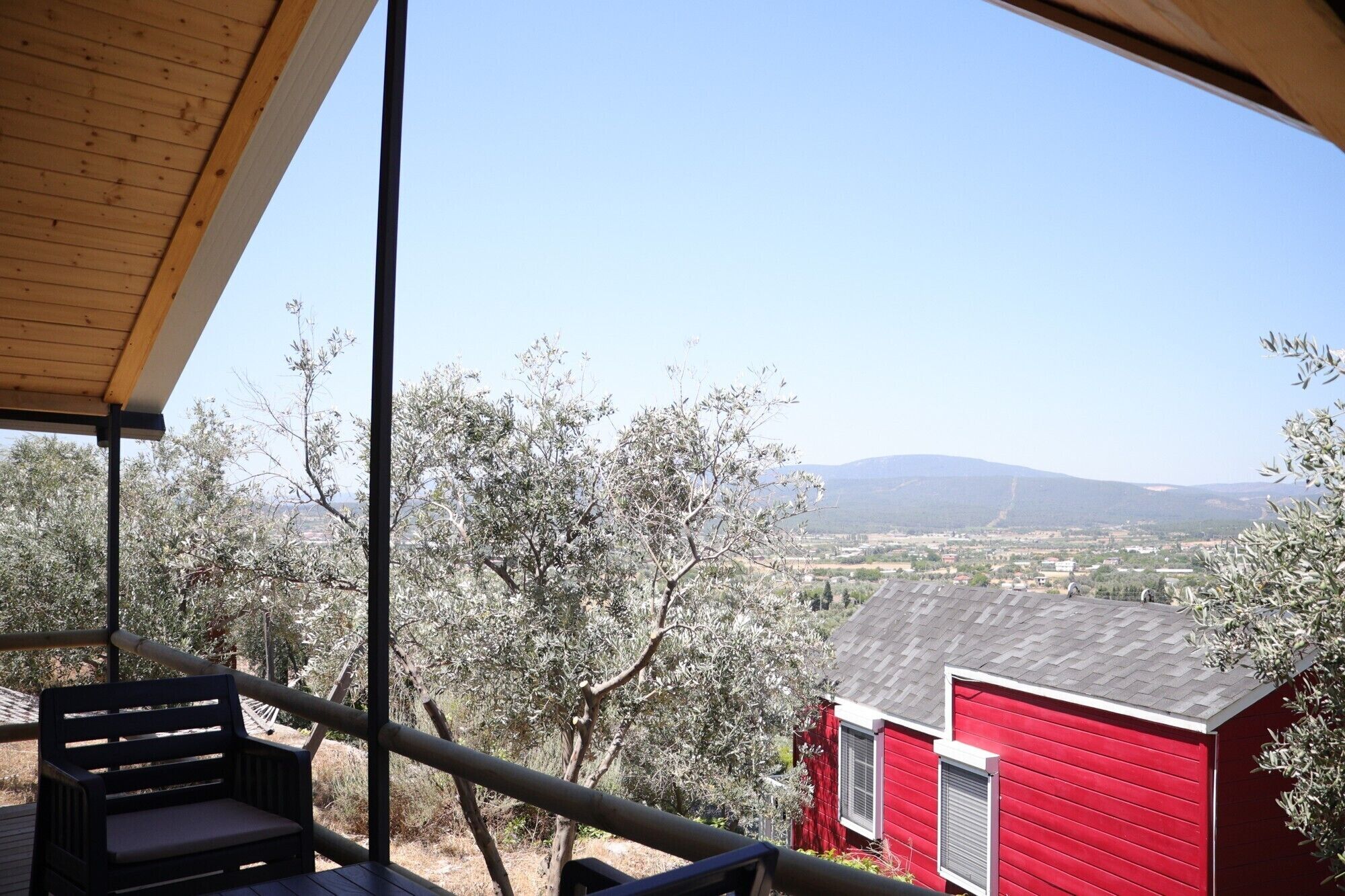 A wooden deck with a bench, overlooking a red building and a valley with trees and distant mountains.