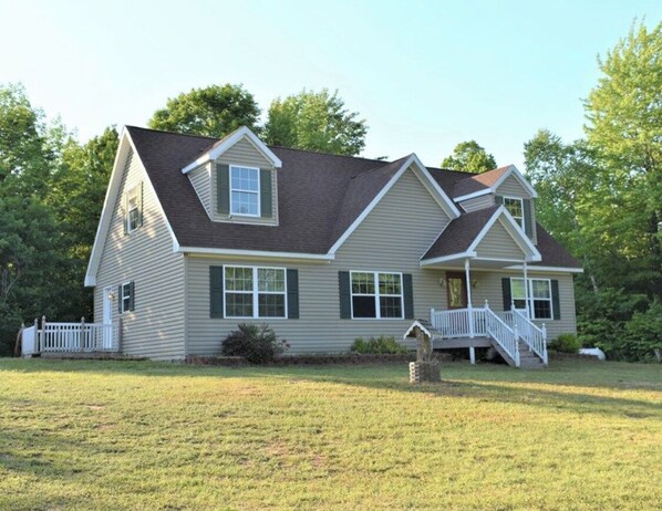 Stunning two-story home with a central entrance, flanked by windows, set amidst a serene lawn and mature trees.