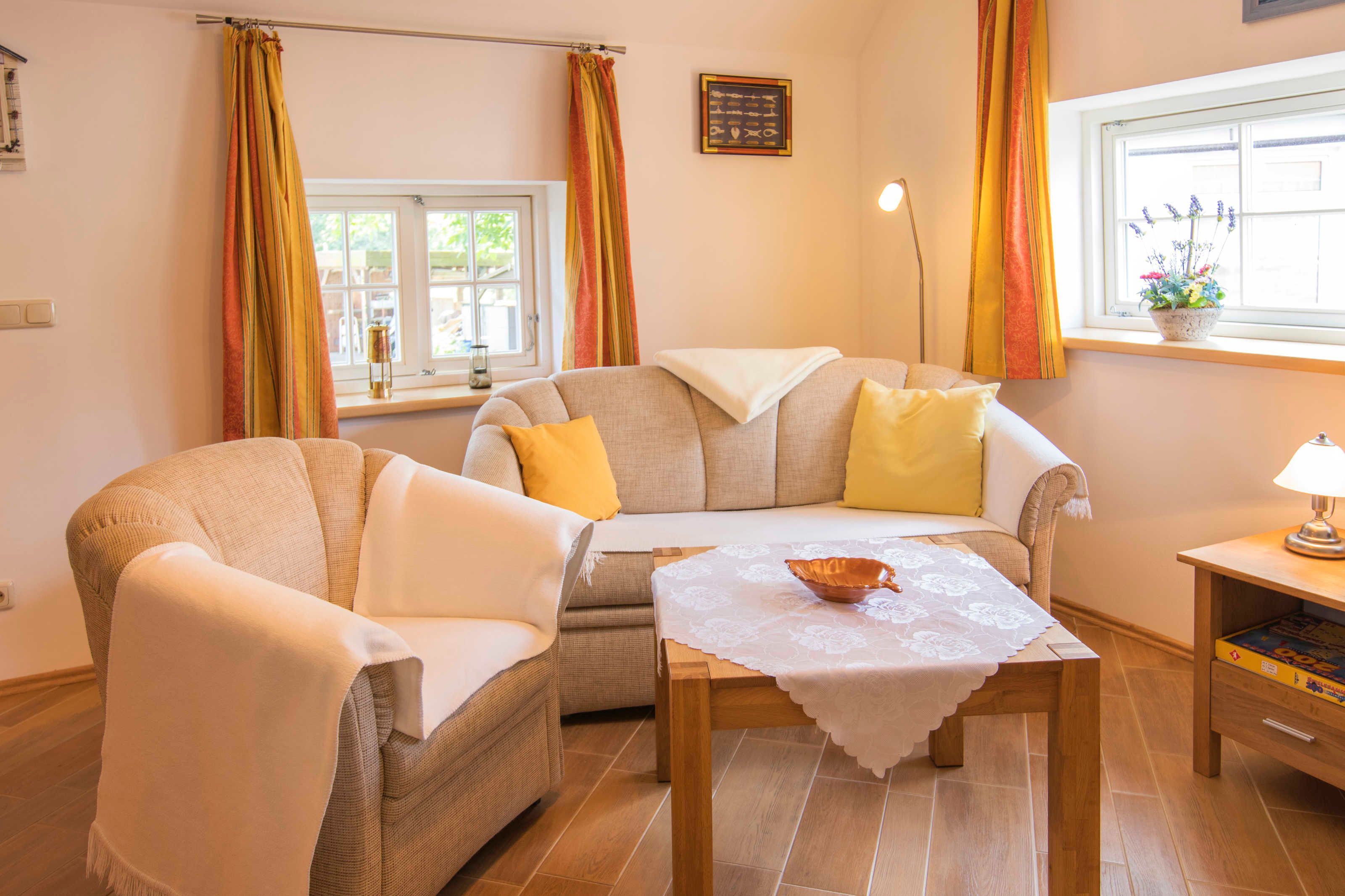 A cozy living room with a sofa, armchairs, a table with a bowl, a lamp, and a window with curtains.