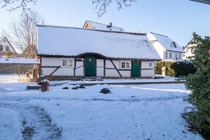 Een traditioneel gebouw met een met sneeuw bedekte dak en een rieten uitbouw.