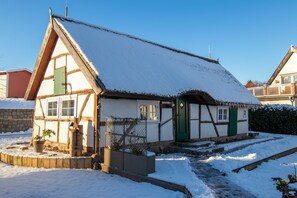 Una casa tradicional con entramado de madera y techo nevado, una puerta verde y un pequeño jardín con macetas.
