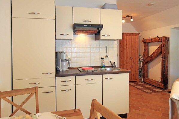 Una cocina compacta con armarios blancos, una cafetera y una pared decorativa de madera.