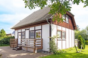 Ein zweistöckiges Haus mit Holzfassade, einer Veranda mit Bank und einem kleinen Garten.