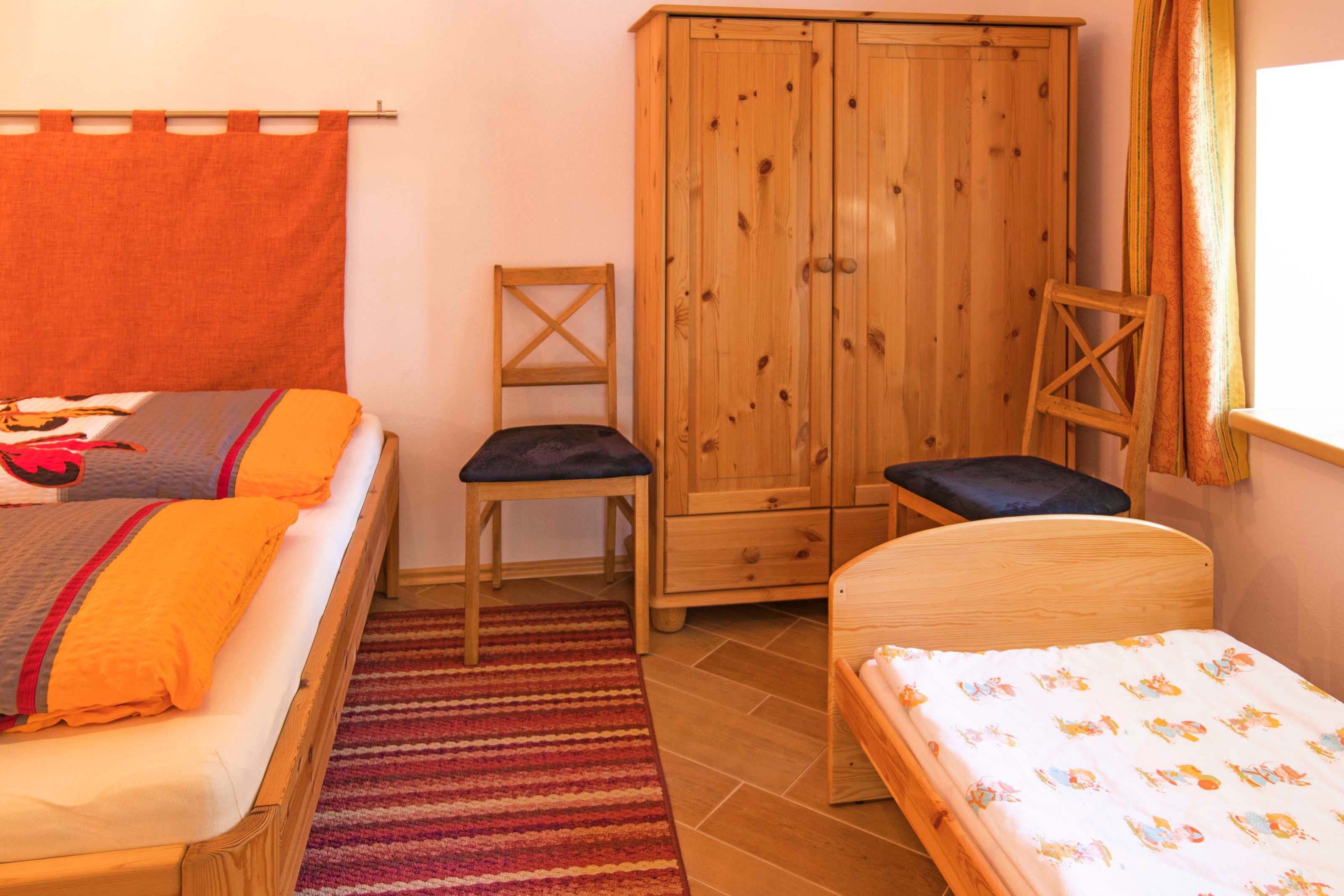 A room with two beds, a wooden wardrobe, a chair, and a window with curtains.