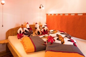 Una cama con ropa de cama estampada con motivos florales, un cabecero de madera y una lámpara fijada a la pared.