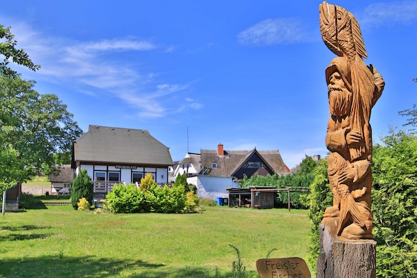 A traditional building with a sloped roof, surrounded by a grassy area and a wooden sculpture. - Ole Koot Vacation Home - Fischerkate Freest (Kroeslin)