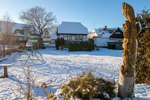 Un espacio exterior cubierto de nieve con una escultura de madera, un edificio con un cartel y un banco.