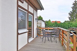 A wooden deck with a table and chairs, a window, and a railing.