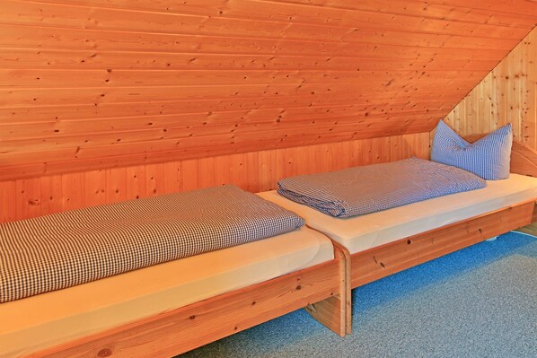 A wooden loft bedroom with two beds, a sloped ceiling, and a blue carpet.