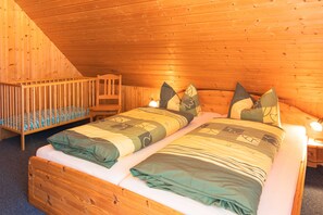 A wooden cabin bedroom with two beds, a crib, and a wooden ladder.