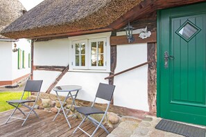 A rustic building with a green door, a thatched roof, and a small outdoor seating area with two chairs and a table.