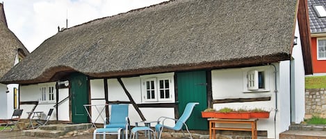 Ett traditionellt hus med halmtak, en träveranda, utomhusmöbler och en liten trädgård.
