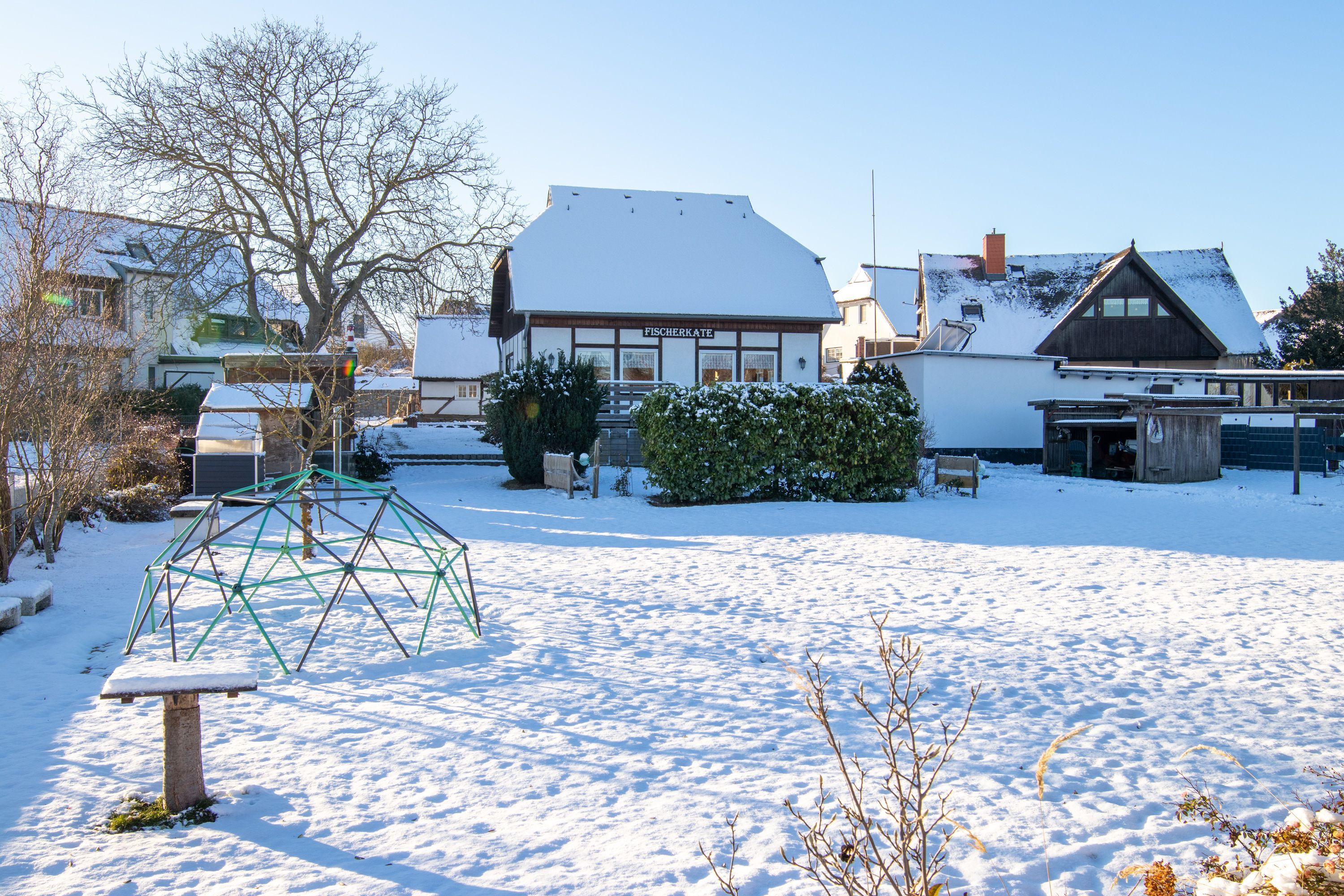 Een besneeuwde buitenruimte met een speeltoestel, een bankje en een gebouw met de tekst 'FISCHERKATE'.