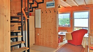Interior de madera con una escalera, una silla roja y vistas al exterior por una ventana.