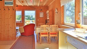 Un interior de madera con zona de comedor, una silla roja, una cocina con lavavajillas y un ventanal con vistas.