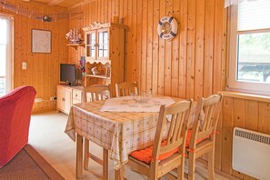 A wooden cabin interior with a dining table, chairs, a television, and a 'Welcome' sign.