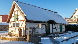 Una casa tradicional con entramado de madera y techo nevado, una puerta verde y un pequeño jardín con macetas.