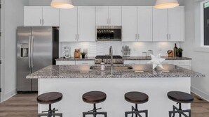 A modern kitchen with white cabinets, a stainless steel refrigerator, a built-in oven, and a granite countertop. There are three bar stools and pendant lights above the island. - Elvis`s Rooftop - Brand New Nashville Hang Out (Nashville)