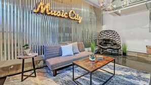 A modern living room with a grey sofa, a wooden coffee table, and a unique hanging chair. A neon sign reads "Music City" on the wall. - Elvis`s Rooftop - Brand New Nashville Hang Out (Nashville)