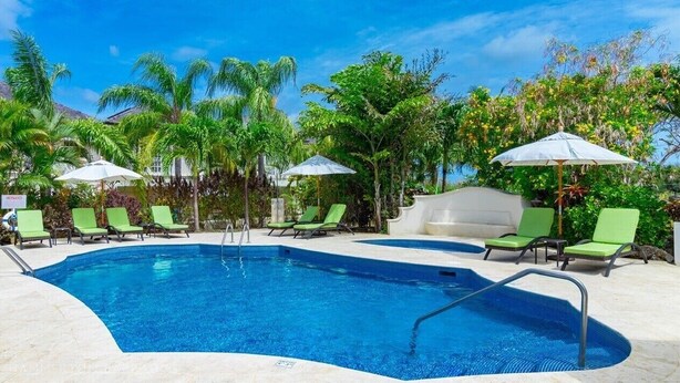 A swimming pool with green lounge chairs and umbrellas, surrounded by tropical vegetation. - Blue Horizon Battaleys Mews - Beautiful villa 5 minutes stroll to Mullins beach (Mullins)