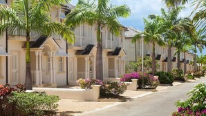 A row of white colonial-style buildings with balconies, surrounded by palm trees and flowering plants. - Blue Horizon Battaleys Mews - Beautiful villa 5 minutes stroll to Mullins beach (Mullins)