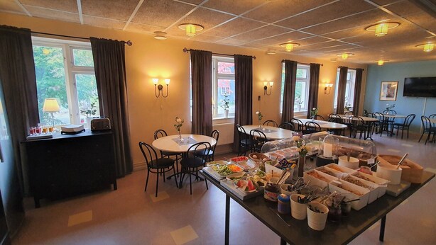 A dining area with multiple tables and chairs, a buffet with various food items, and a television mounted on the wall. - Nipanhotellet (Solleftea)