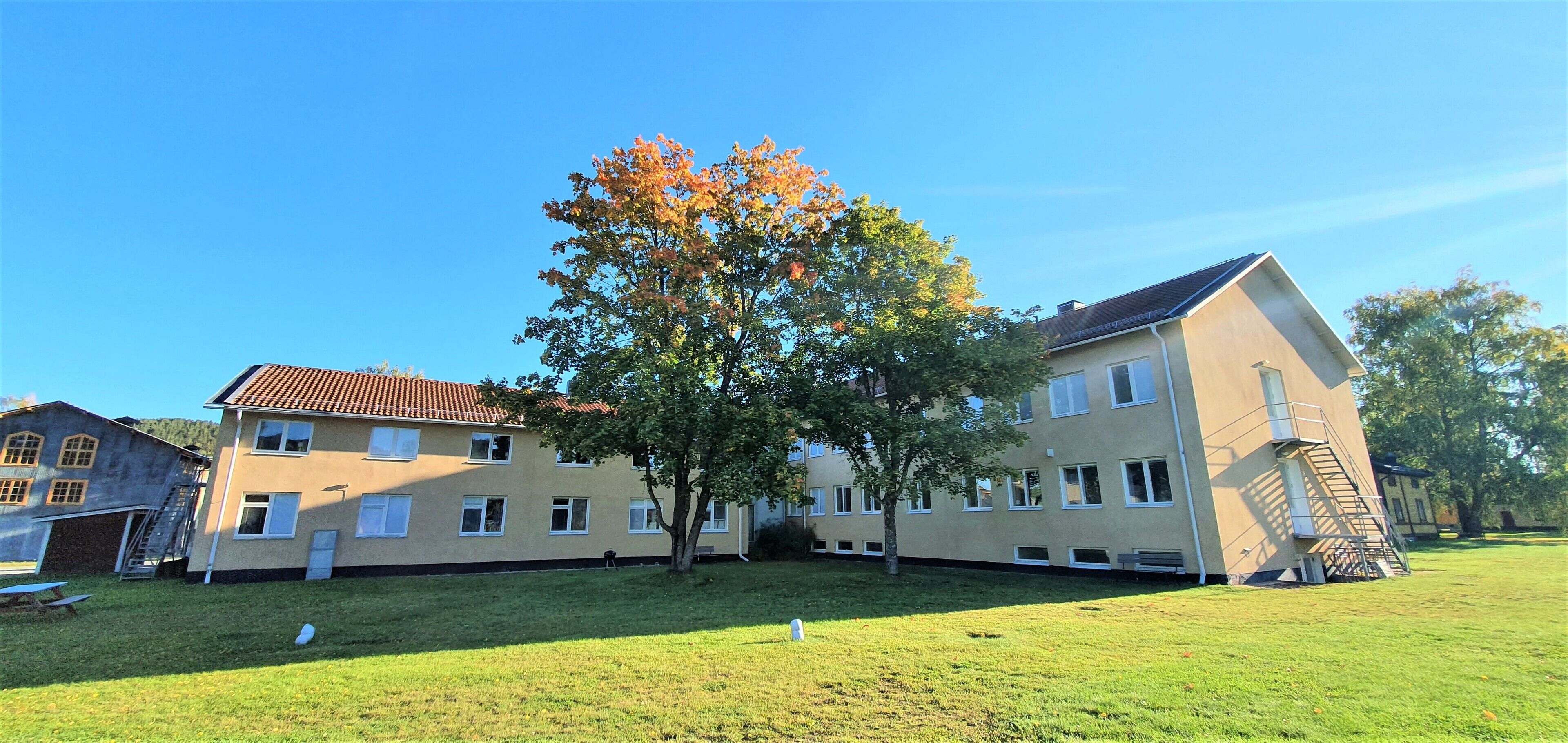 Ein mehrgeschossiges Gebäude mit flachem Dach, einem zentralen Innenhof und einem Baum mit Herbstlaub.